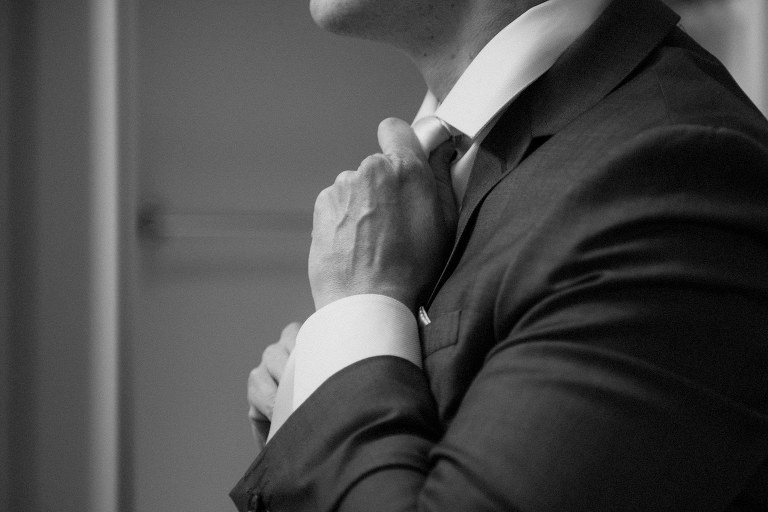 closeup of groom adjusting tie,